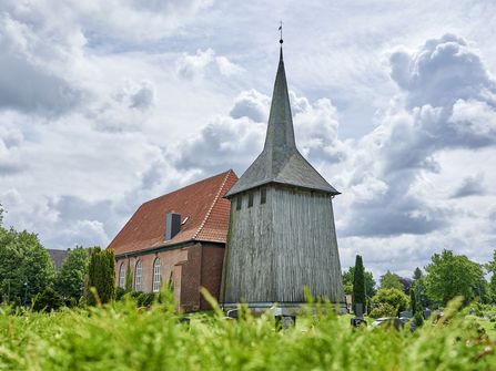 Sicht von schräg vorne auf die Kirche mit Holzturm und Steinbau